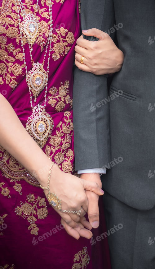 Preview: Bride holding groom's hand close up photo. Gold Jewelry and purple homecoming dress.