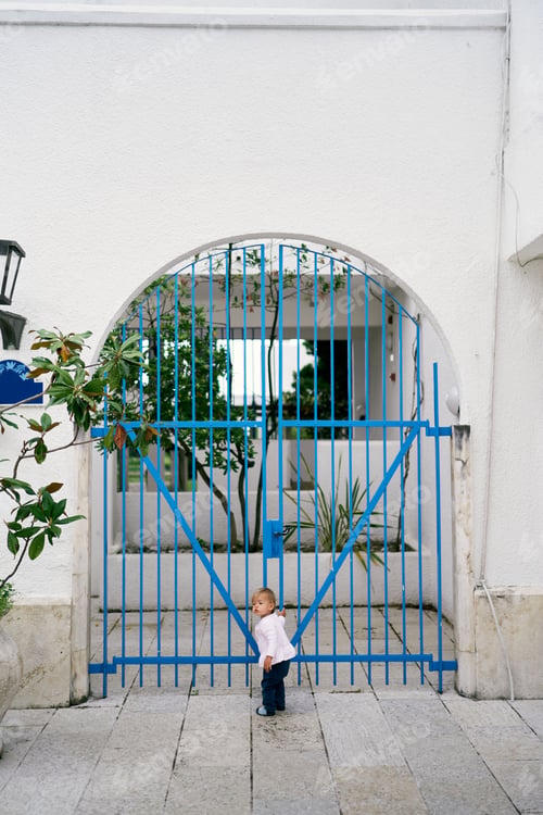 Preview: Kid stands in the courtyard of the house and holds his hand to the lattice gate
