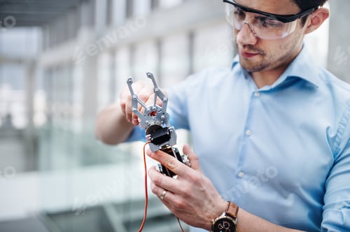 Preview: A young businessman or scientist with robotic hand standing in office, working.