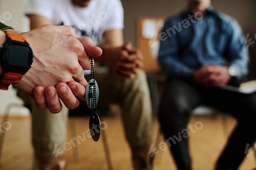 Preview: Hands with clasped fingers of young depressed man with two medallions on chain