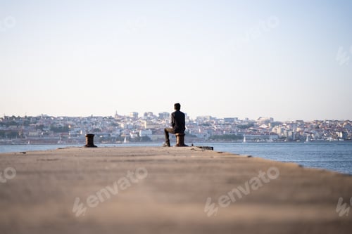 Preview: Back of a man sitting facing the river and the city scape in a sunny day