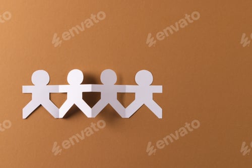 Preview: Close up of four paper cut out people figures holding hands with copy space on brown background