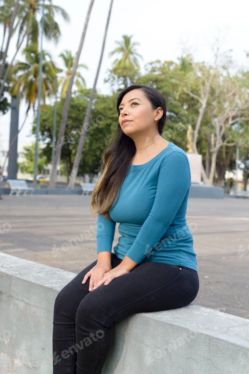 Preview: Woman seated in a public park with an attitude of preoccupation, pensive.