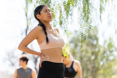 Preview: Hispanic young woman expresses back pain while doing sports