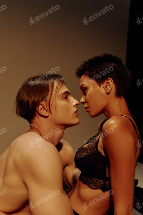 Preview: side view of shirtless muscular man and hot woman in black bra looking at each other on brown