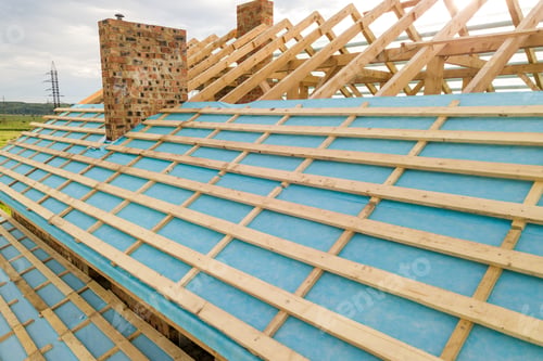 Preview: Aerial view of a brick house with wooden roof frame under construction.