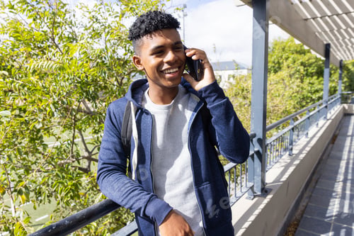 Preview: Hanging out, male student smiling and talking on smartphone outdoors