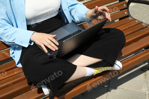 Preview: The girl works on a laptop while sitting on a bench
