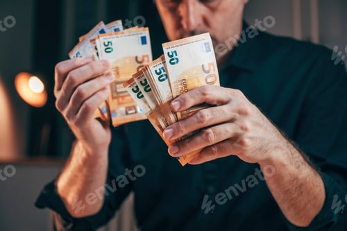 Preview: Businessman counting fifty euro banknotes in office while working overtime