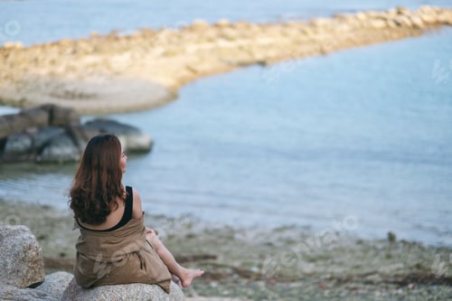 Preview: A beautiful asian woman enjoy sitting on the rock by the seashore