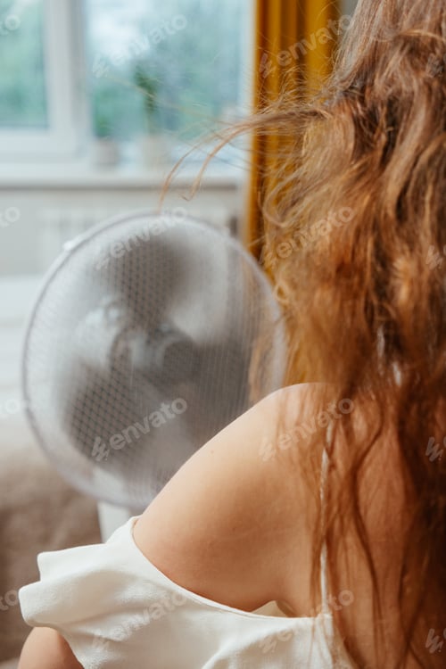 Preview: view from back Fan cools Caucasian woman languishing in summer heat.