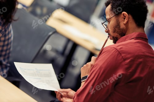Preview: Young mixed race man analyzing document while working in the modern office, selective focus