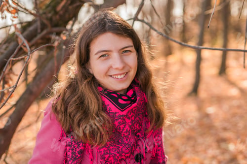 Preview: Cheerful young woman with pink scarf relaxing at park with yellow trees in background copy space