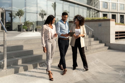 Preview: Group of Multiracial business people walking, talking and using a tablet outside office building