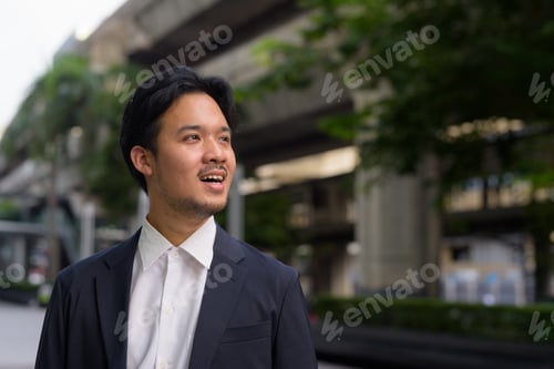 Preview: Portrait of Asian businessman outdoors in the city smiling and thinking