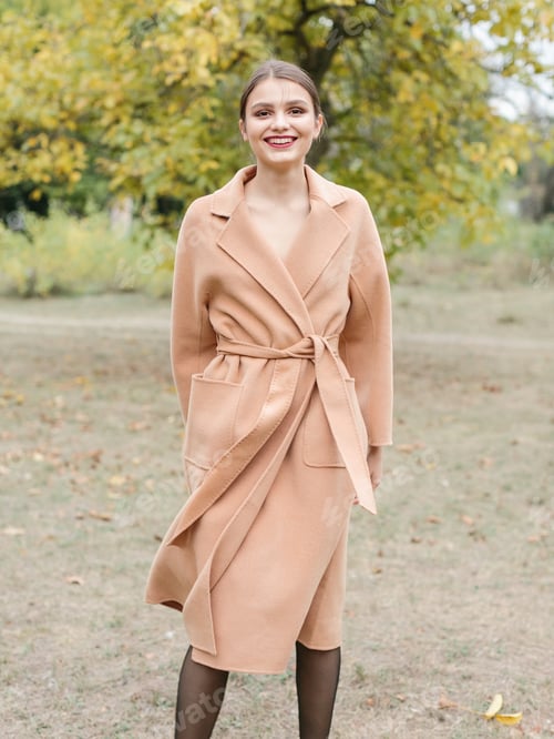 Preview: Woman with brown hair in a long trench coat walking on the park.