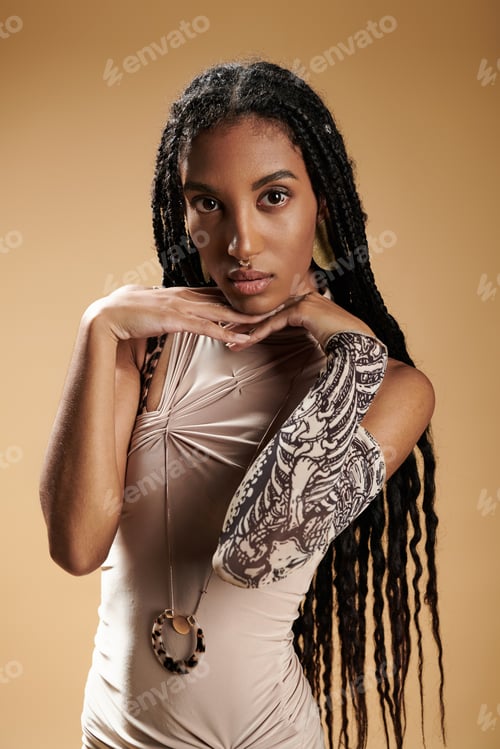 Preview: A stylish young woman poses gracefully, highlighting her distinctive tattoo and confident demeanor