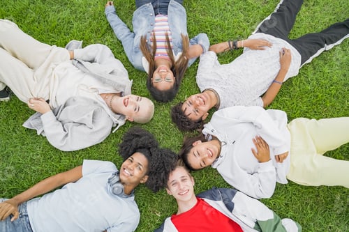 Preview: Group of multiethnic friends laying down in a circle on the grass in the park