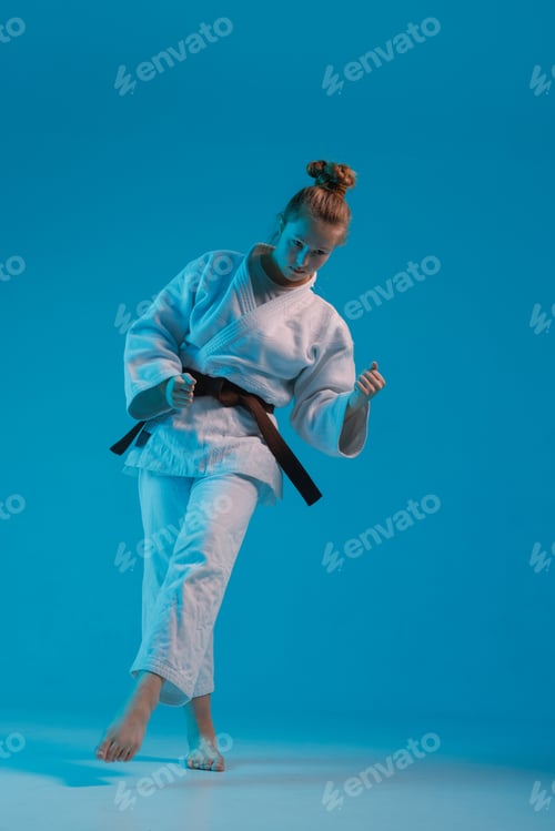 Preview: girl judoka in a white kimano with a black belt on a blue background, studio photo