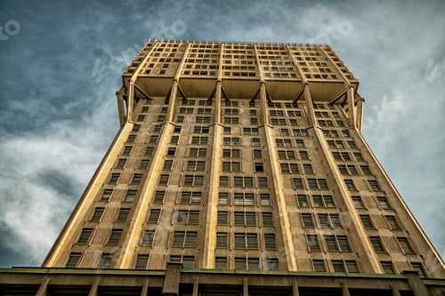 Preview: Upward view of a tall Torre Velasca tower in Brutalist style building against a clear blue sky