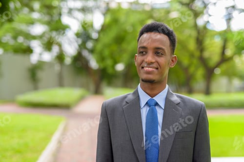 Preview: Portrait of handsome African businessman wearing suit and tie at park outdoors