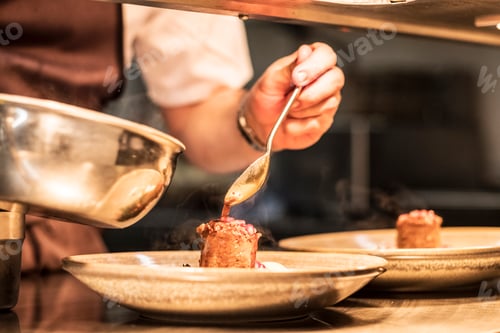 Preview: Close up of chef in commercial kitchen holding spoon, drizzling sauce on plate.