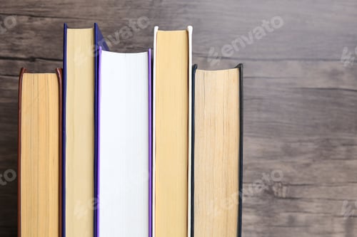 Preview: Collection of different books near wooden wall, closeup. Space for text