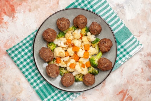 Preview: top view broccoli and cauliflower salad and meatball on plate green and white checkered napkin on