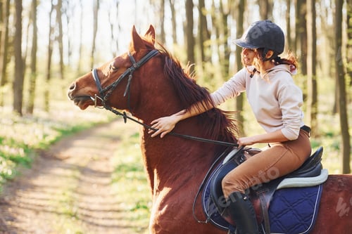 Preview: Young woman in protective hat with her horse in the forest at sunny daytime