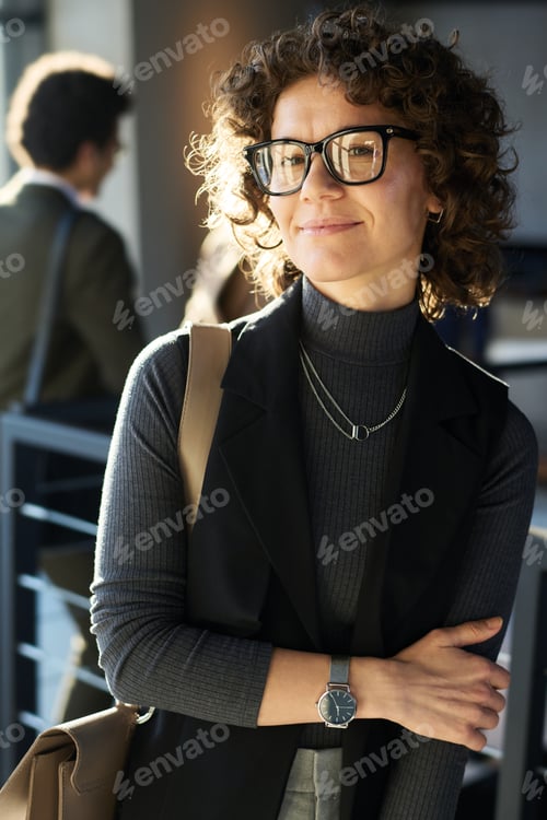 Preview: Young curly brunette female manager in smart casualwear and eyeglasses