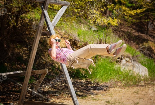 Preview: Senior woman joyfully swinging on a swing and having fan