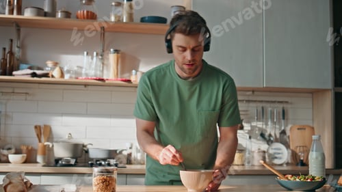 Preview: Funny guy cooking meal in earphones dancing kitchen closeup. Man listening music