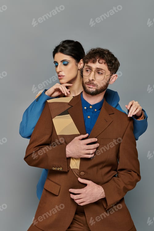 Preview: stylish man and woman in suits posing on grey background, elegant style, formal wear, bold makeup