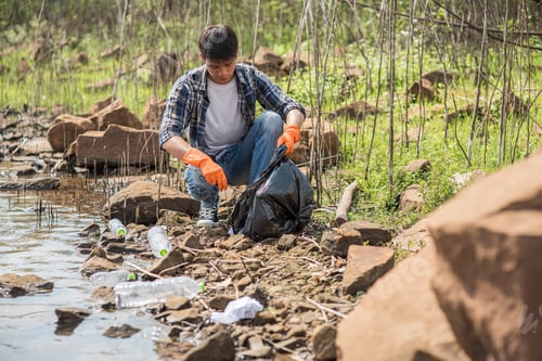 Preview: A man wearing orange gloves collecting garbage in a black bag.