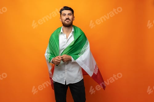 Preview: Portrait of a young casual man holding flag of Iran against orange background