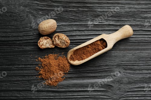 Preview: Scoop with nutmeg powder and seeds on black wooden table, flat lay