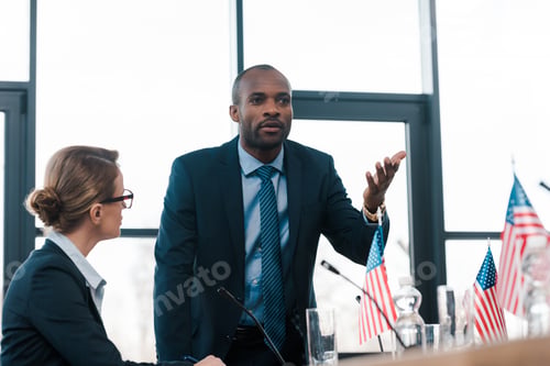 Preview: selective focus of attractive diplomat looking at african american man gesturing while talking near