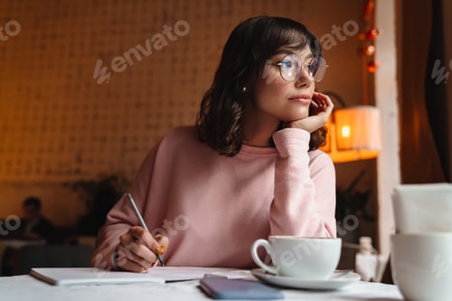 Preview: Brunette young woman indoors in cafe writing notes