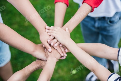 Preview: Cropped shot of children stacking hands while standing on green grass