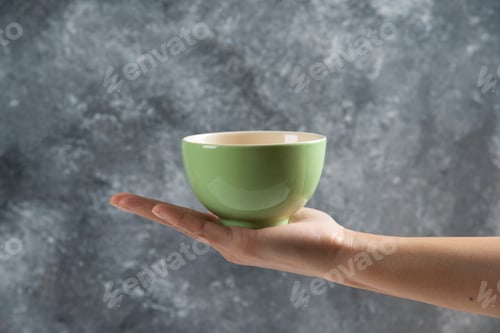 Preview: Female hand holding a green bowl on a gray background