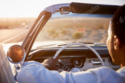 Preview: Rear View Of Man On Road Trip Driving Classic Convertible Car Towards Sunset