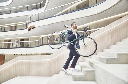 Preview: Businesssman carrying bicycle in modern office building