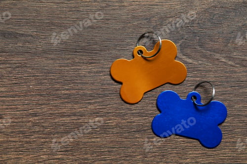 Preview: Color metal pet tags in shape of bones with ring on wooden table, flat lay. Space for text