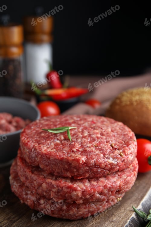 Preview: Raw hamburger patties with rosemary on wooden board, closeup