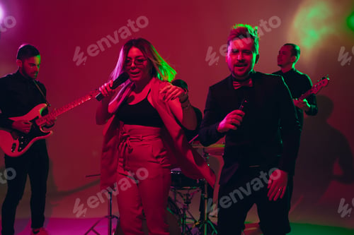 Preview: Young caucasian musicians, band performing in neon light on red studio background