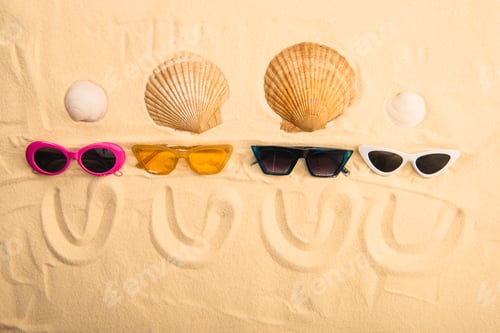 Preview: top view of sunglasses and seashells with smiles drawn on sand