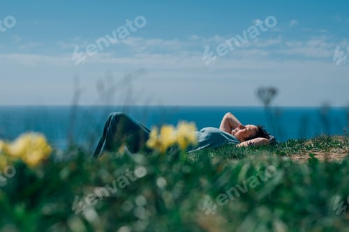 Preview: adult woman with a smile lies on the grass in the summer against the background of the sea, sky