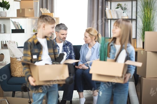 Preview: Smiling kids with moving boxes posing at new flat with parents behind
