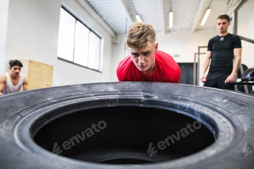 Preview: Fit young man with friends in gym working out, moving tire.