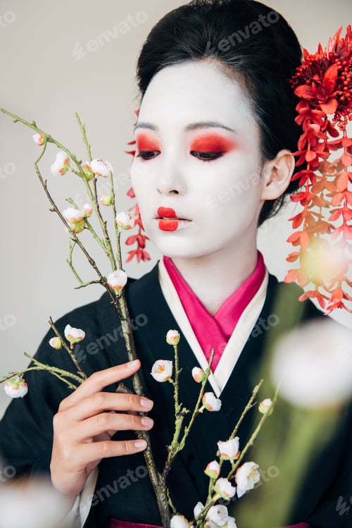 Preview: selective focus of tree branches and beautiful geisha with red and white makeup isolated on white